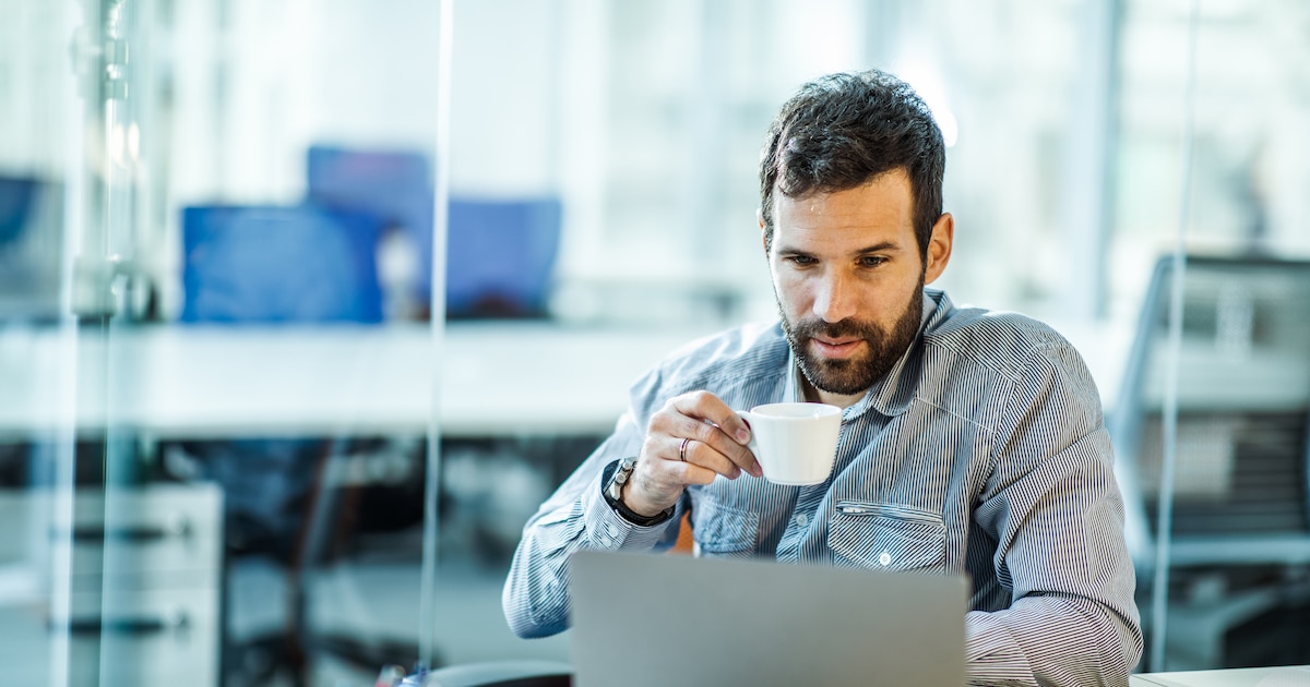 Male entrepreneur reading an e-mail on his computer while drinking coffee.